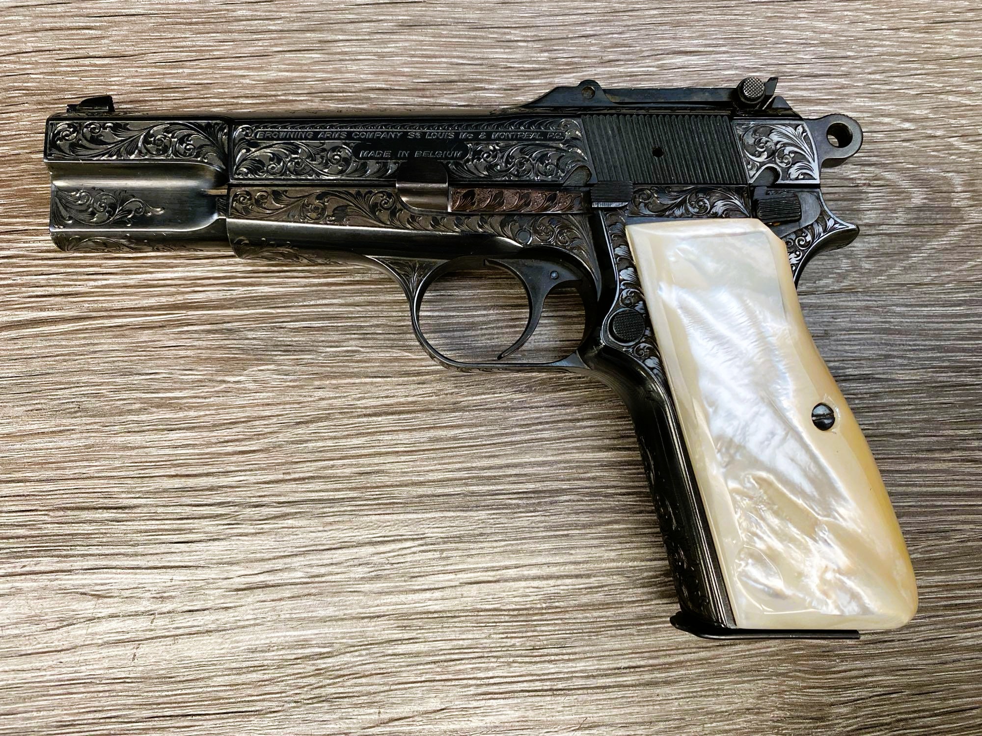 Factory-engraved Belgian Browning Hi-Power 9mm semi-automatic pistol with a blue finish, faux pearl grips, and a leather boot case.