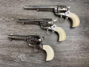 Set of three engraved Colt Custom Workshop 3rd Generation Single Action Army revolvers with nickel finish, white grips, and a factory presentation case.